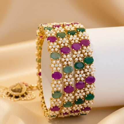 Set of 4 wide gold-tone bangles with alternating ruby and emerald oval zircon stones in white seed pearl halos – copper/brass fashion jewelry